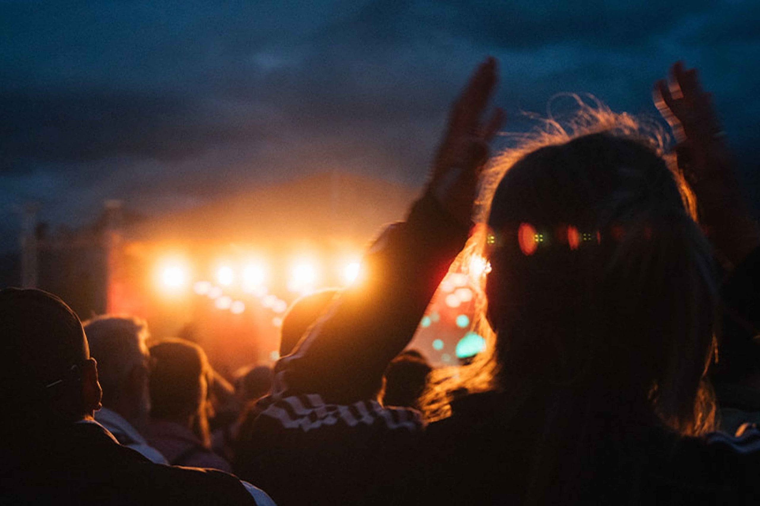 Publikum sitzt bei Open-Air-Konzert vor Bühne, Gebäude im Hintergrund, Abendstimmung