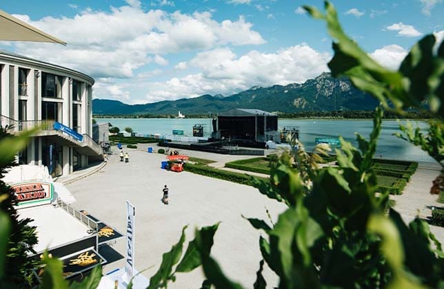 Blick auf Bühne und Berge am Seeufer bei Konzert, sonniges Wetter, grüne Pflanzen