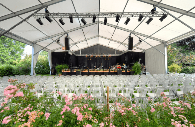 Überdachte Bühne mit Stuhlreihen und Blumen im Vordergrund im Garten.